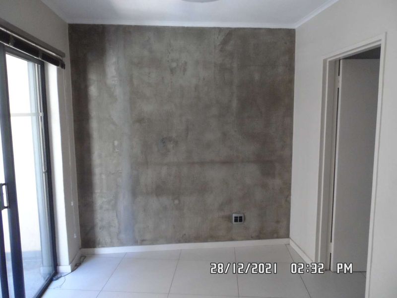 An empty bedroom featuring tiled flooring, a sliding glass door, and an unfinished concrete feature wall.