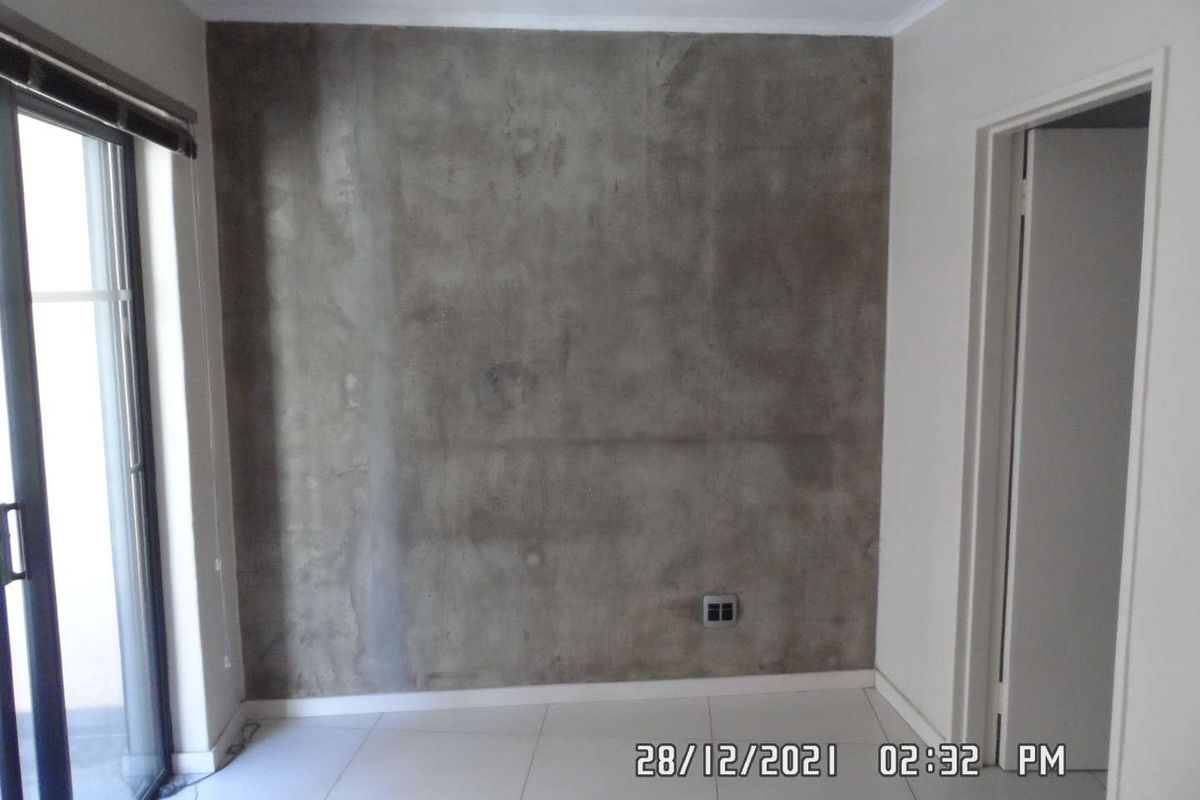 An empty bedroom featuring tiled flooring, a sliding glass door, and an unfinished concrete feature wall.