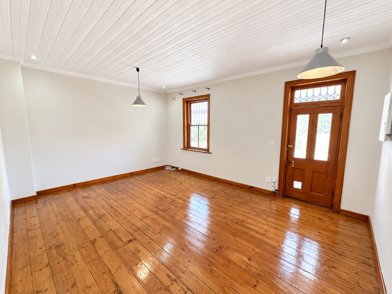 A bright, empty living room featuring polished timber flooring, a timber-framed door with glass panels, and a classic tongue and groove ceiling.
