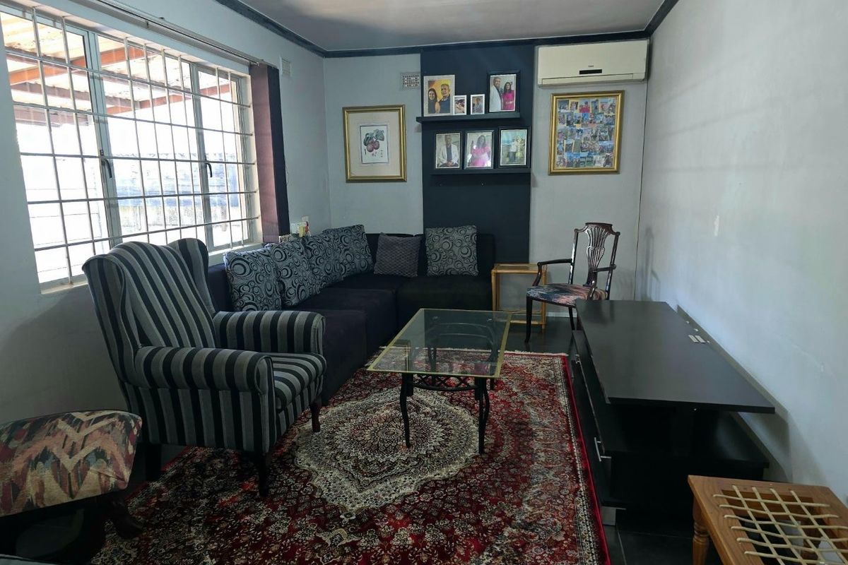 A comfortable living room featuring tiled flooring, an integrated air conditioning unit, and large windows fitted with security bars.