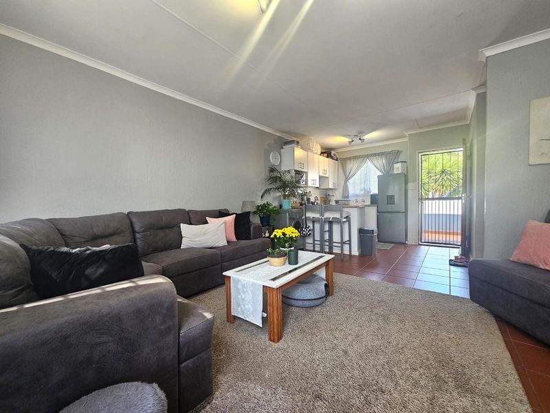 Open plan living area featuring a combined kitchen with cabinetry and tiled floors, transitioning into a carpeted lounge space with access to an exterior door.