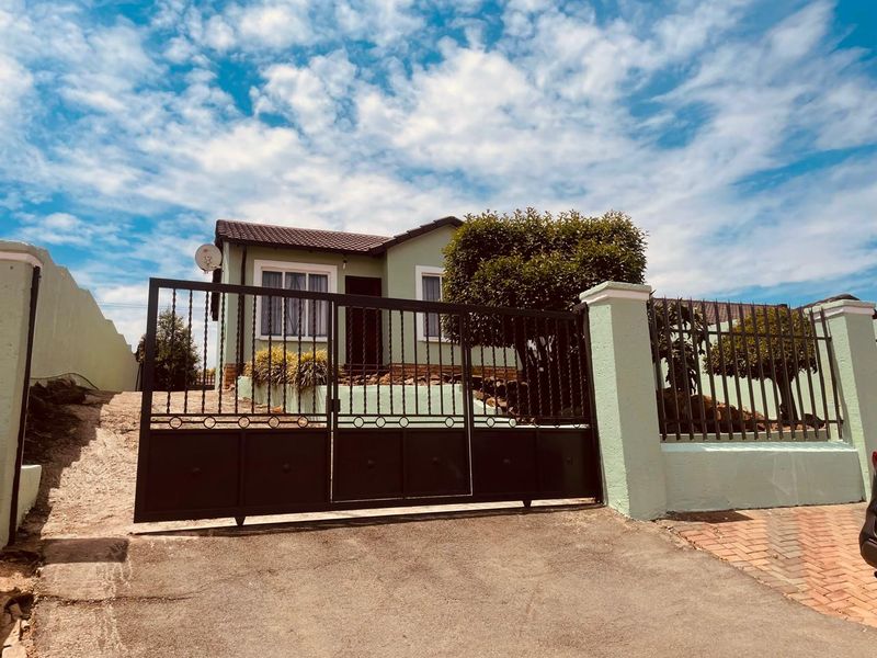 Front exterior view of a single-story house featuring a secure metal driveway gate, perimeter wall, and a paved driveway.