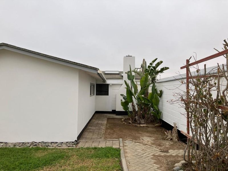 Rear exterior view of the property featuring a paved walkway, masonry boundary wall, and an external chimney stack.