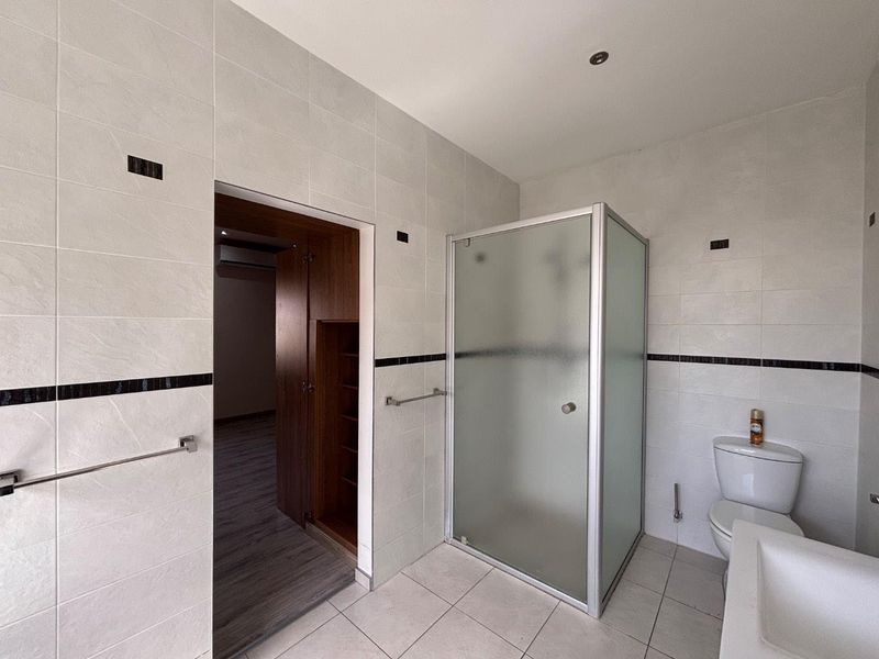 A functional bathroom featuring a shower enclosure, toilet, and neutral wall tiling, currently vacant and ready for minor cosmetic updates.