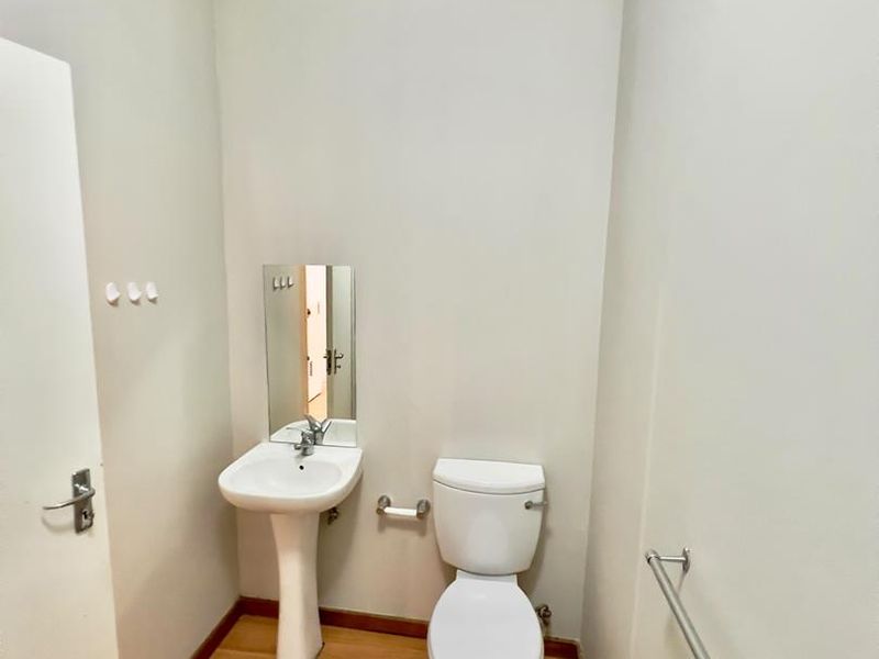 A compact guest bathroom featuring a pedestal basin, toilet, and laminate flooring, providing a functional and clean space.