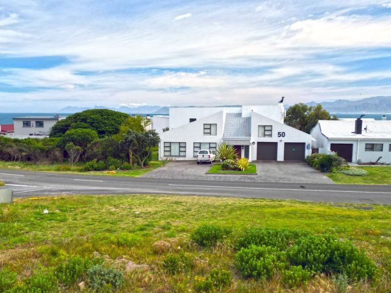An elevated aerial view of a residential property featuring a double garage, paved driveway, and scenic coastal mountain backdrop.