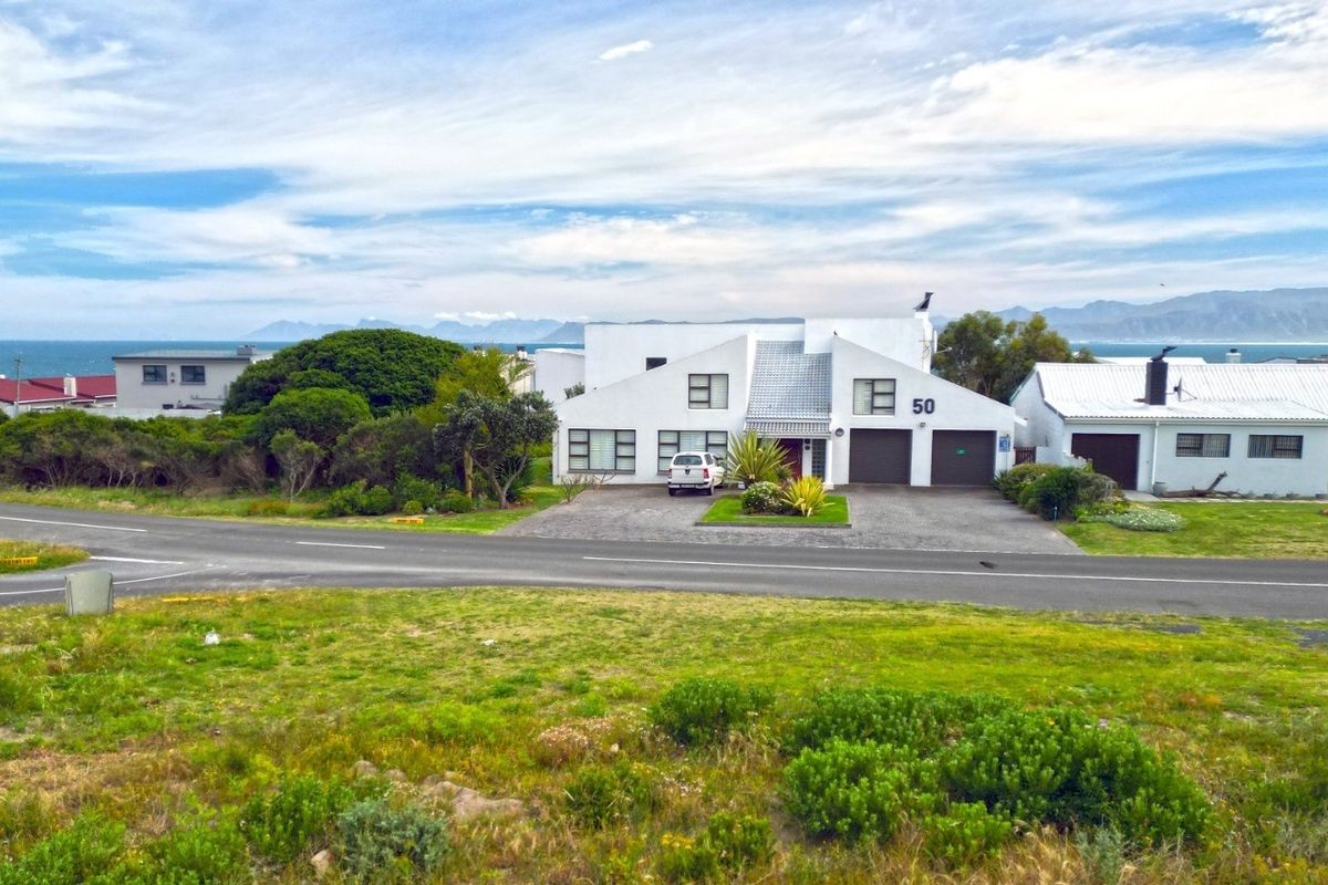 An elevated aerial view of a residential property featuring a double garage, paved driveway, and scenic coastal mountain backdrop.