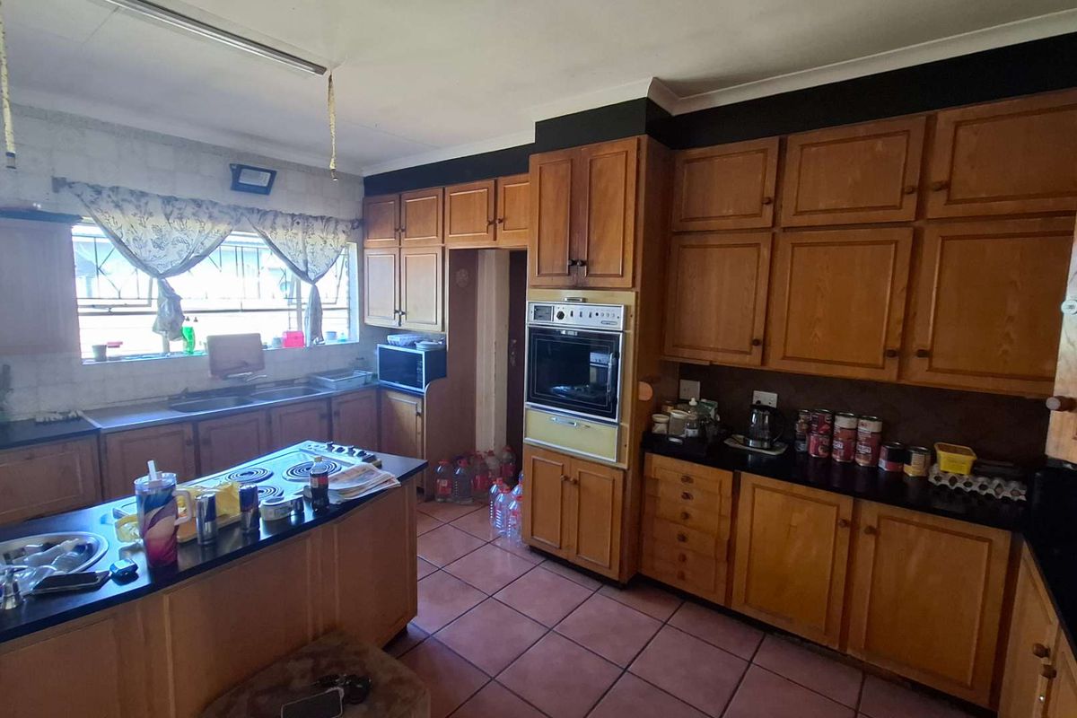 A spacious kitchen featuring extensive wooden cabinetry, black granite countertops, an integrated oven, and a central island with an electric hob.