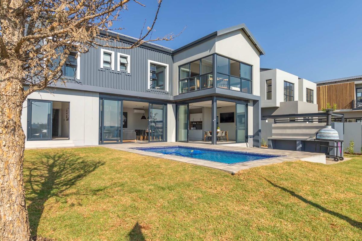 Modern double-story residence featuring a rear garden, swimming pool, and expansive glass sliding doors connecting the interior living spaces to the outdoor area.