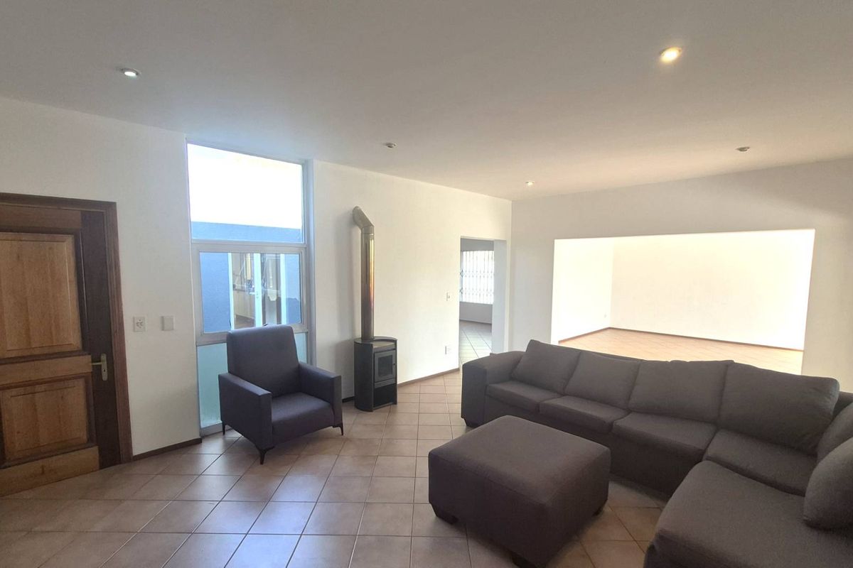 Spacious living area featuring tiled flooring, recessed ceiling lighting, and a built-in fireplace, with an open-plan layout leading to an adjacent room.