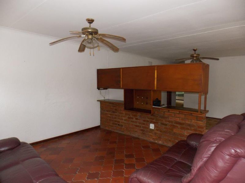 A living area featuring a brick room divider with built-in wooden cabinetry, ceiling fans, and traditional terracotta floor tiles.