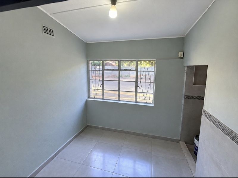 A clean, empty bedroom featuring neutral tiled flooring, a large window with security bars, and a simple, functional layout ready for personalization.