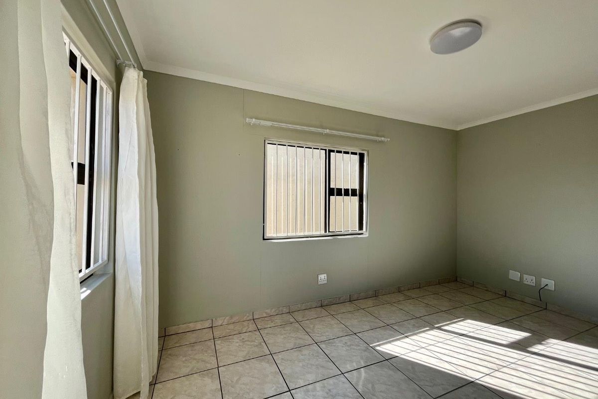 A bright, empty bedroom featuring neutral wall paint, tiled flooring, and security bars on the windows.