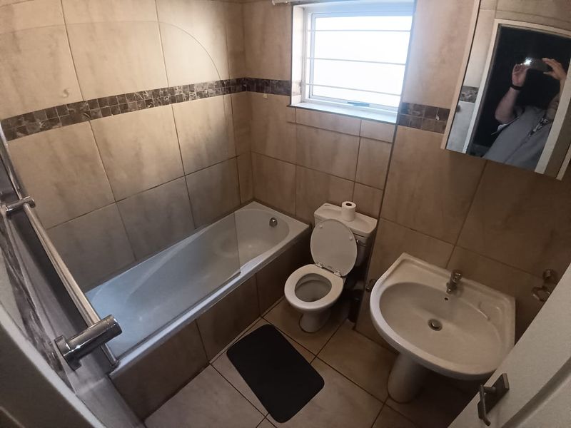 A functional bathroom featuring a bathtub with a glass screen, pedestal basin, toilet, and neutral wall and floor tiling.