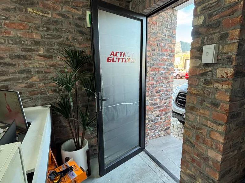 Entrance area featuring exposed brick walls and an aluminium framed glass door with branding.