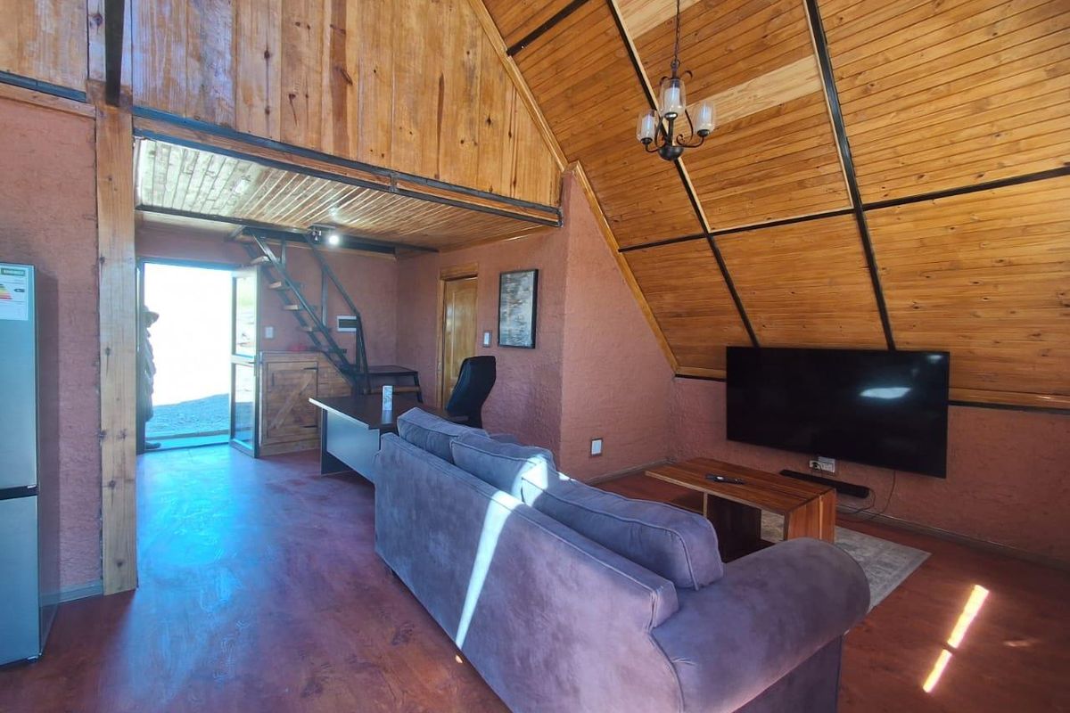 Spacious living area featuring high exposed timber ceilings, textured walls, and a metal staircase leading to an upper level.