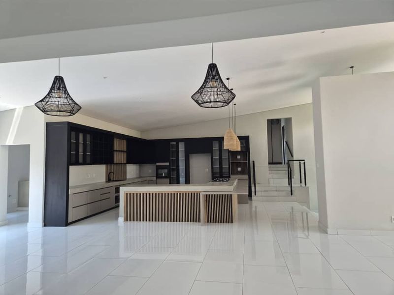 Spacious open-plan kitchen featuring modern dark cabinetry, a central island with slatted detailing, and sleek tiled flooring, seamlessly integrated with a staircase area.