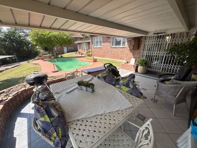 A covered outdoor patio area featuring tiled flooring and a security gate, overlooking a private swimming pool and garden space.