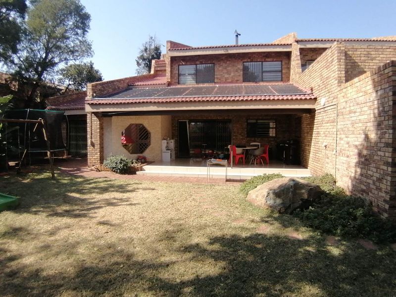 Rear view of a face brick house featuring a covered patio, solar panels on the roof, and a spacious garden area.