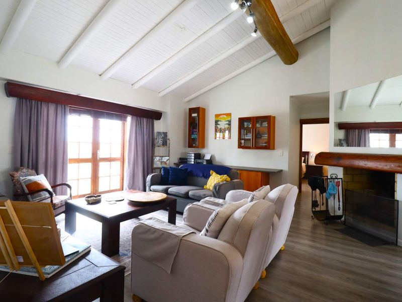 Spacious living room featuring a vaulted ceiling with exposed timber beam, a fireplace with a timber mantel, and direct access to the outdoors via french doors.