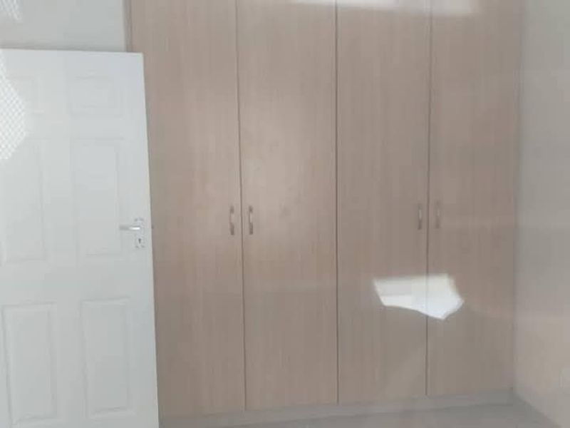 A clean, empty bedroom featuring light wood-finish built-in cupboards and a standard white internal door.
