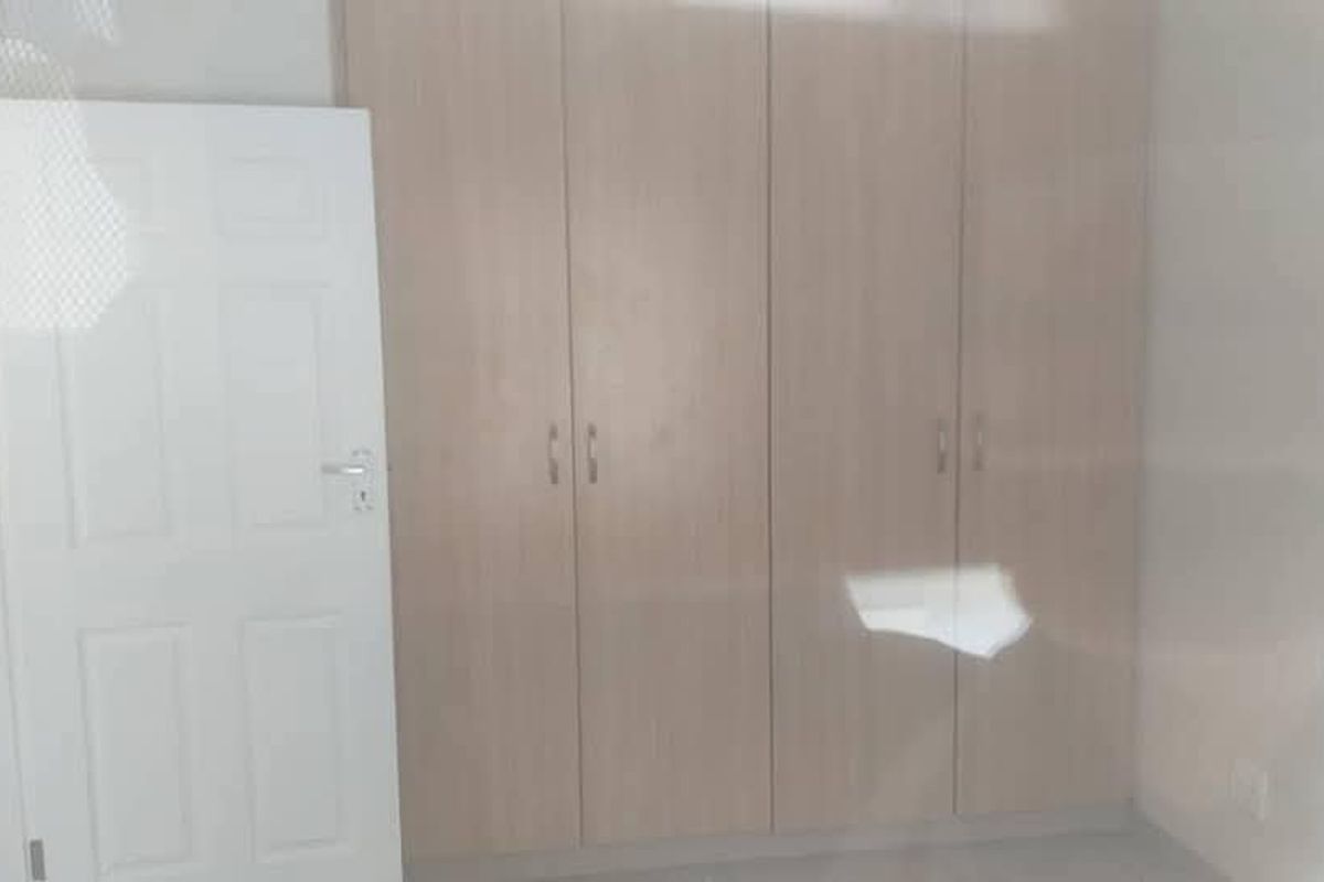A clean, empty bedroom featuring light wood-finish built-in cupboards and a standard white internal door.