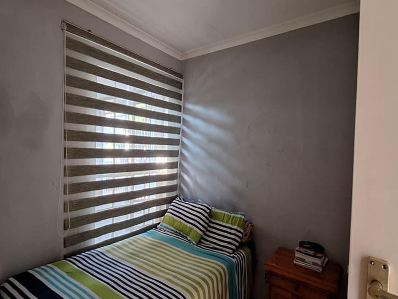 A compact bedroom featuring grey walls, coving, and a window fitted with modern zebra blinds.
