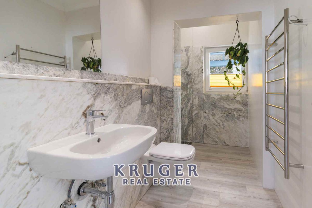 Modern bathroom featuring high-end marble wall tiling, a wall-mounted basin, a concealed cistern toilet, and a stainless steel heated towel rail.