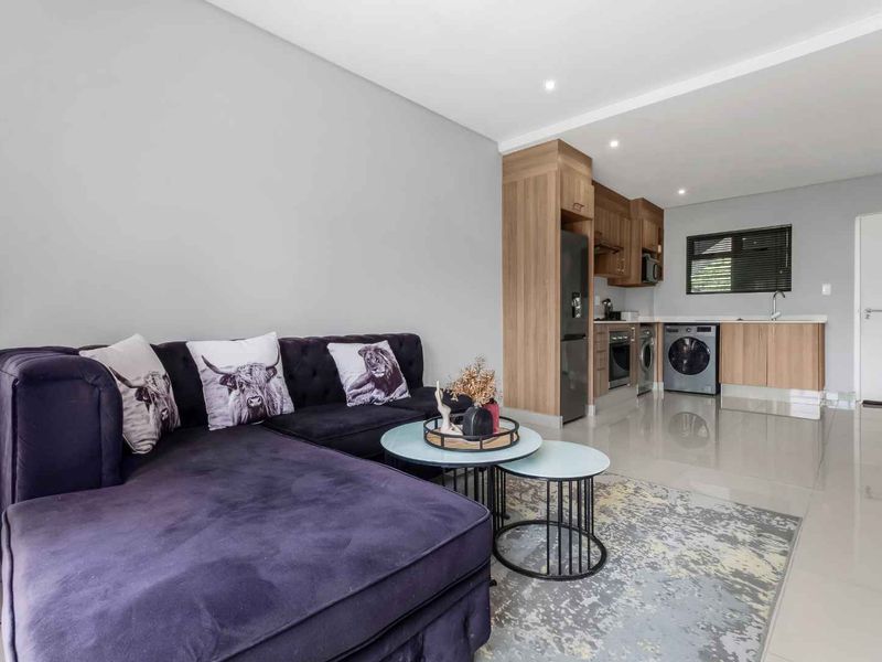 Modern open-plan living area featuring a sleek kitchen with built-in cabinetry, integrated appliances, and polished tiled flooring throughout.