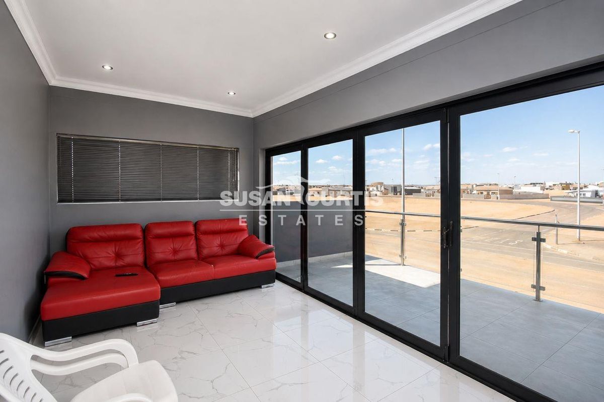 Modern living area featuring large black-framed sliding glass doors that open onto a balcony with tiled flooring and recessed ceiling lighting.