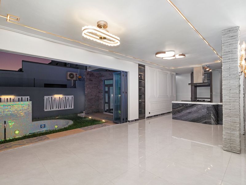 Spacious open-plan living and kitchen area featuring a marble island, modern lighting, and seamless indoor-outdoor flow through large stacking doors to the pool area.
