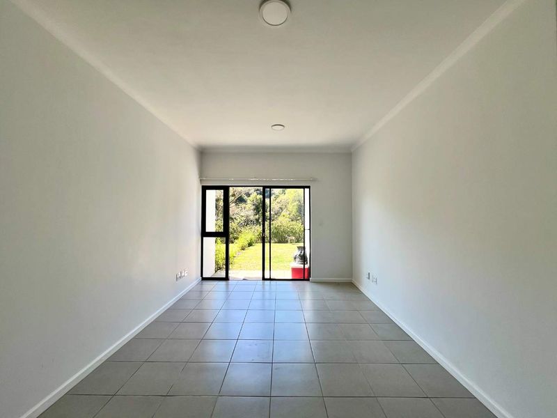 A bright, empty living room featuring neutral tiled flooring and a large sliding glass door providing direct access to the garden.