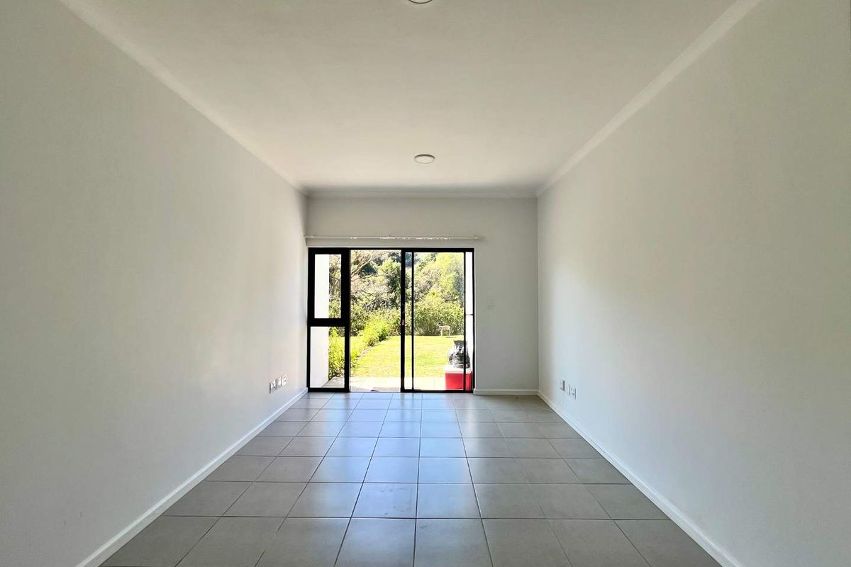 A bright, empty living room featuring neutral tiled flooring and a large sliding glass door providing direct access to the garden.