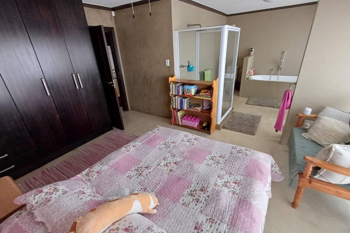 Spacious bedroom featuring built-in dark wood cabinetry and an open-plan en-suite bathroom with a glass shower enclosure and a built-in bathtub.