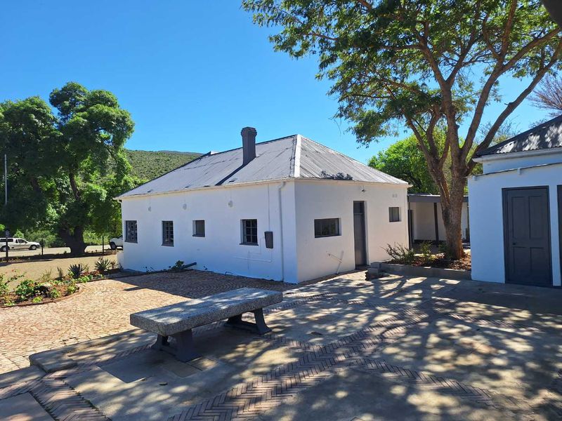 A well-maintained rear exterior view of the guest house featuring a paved courtyard, stone bench, and traditional corrugated metal roof.