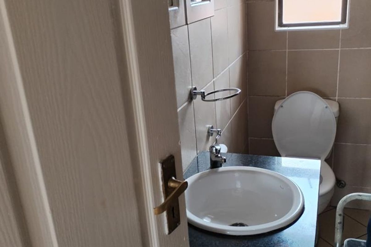 A compact bathroom featuring a vanity with a granite countertop, integrated basin, and a standard toilet, finished with neutral wall tiling.