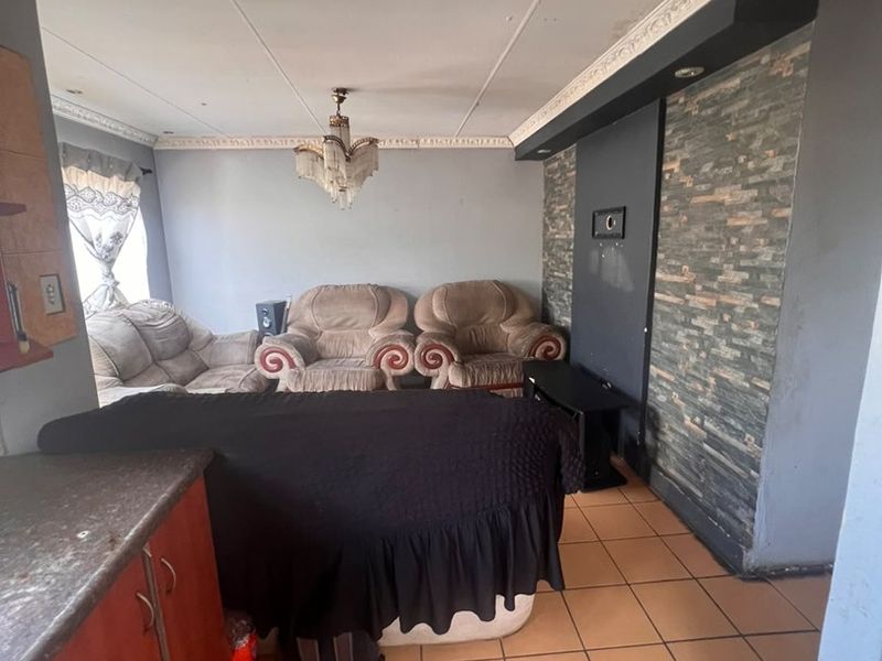 Open plan living area featuring tiled flooring, a stone veneer feature wall, and decorative ceiling cornices, offering potential for modernization.
