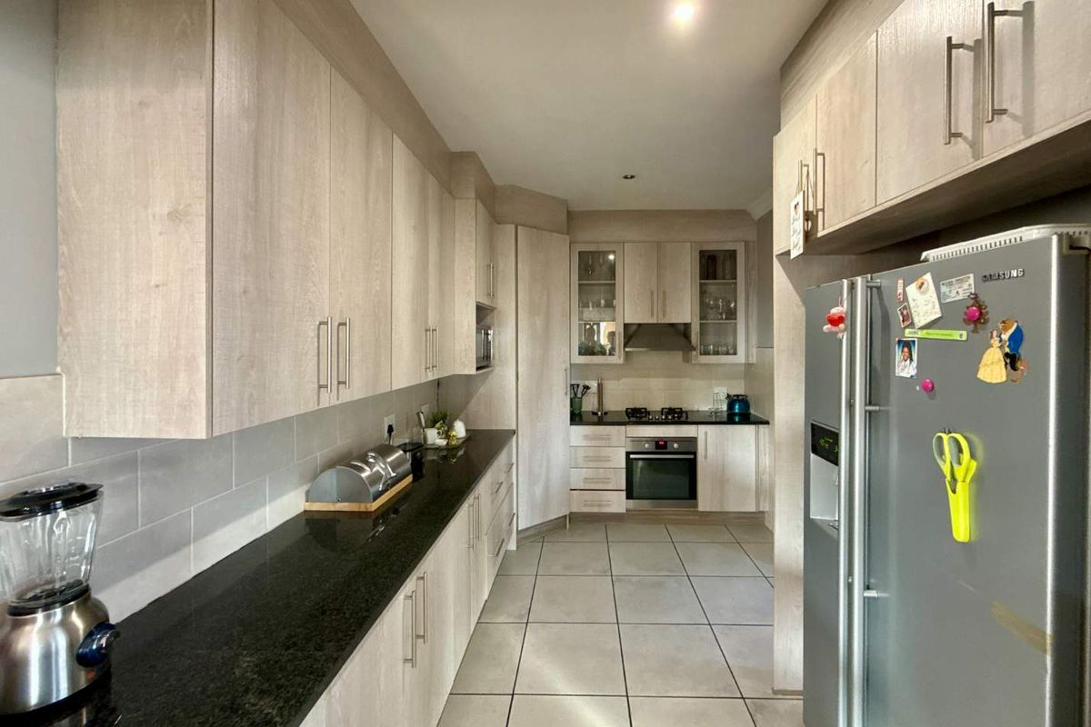 Modern kitchen featuring light wood-grain cabinetry, dark granite countertops, built-in oven, gas hob, and neutral floor tiles.