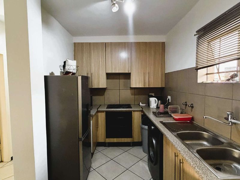 Functional kitchen featuring wood-look cabinetry, laminate countertops, a double basin sink, built-in oven, and hob with tiled backsplash and flooring.