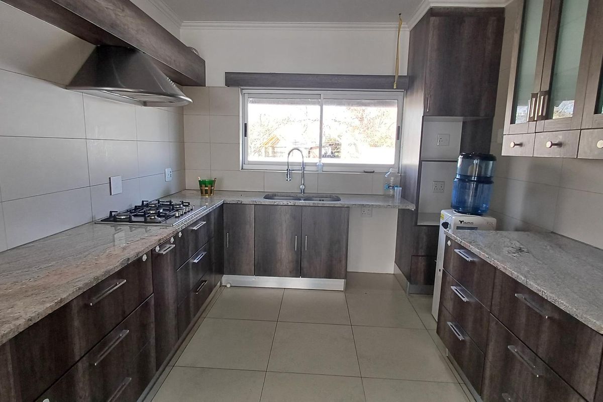 Modern kitchen featuring dark wood cabinetry, granite countertops, a gas hob with extractor fan, and tiled flooring throughout.