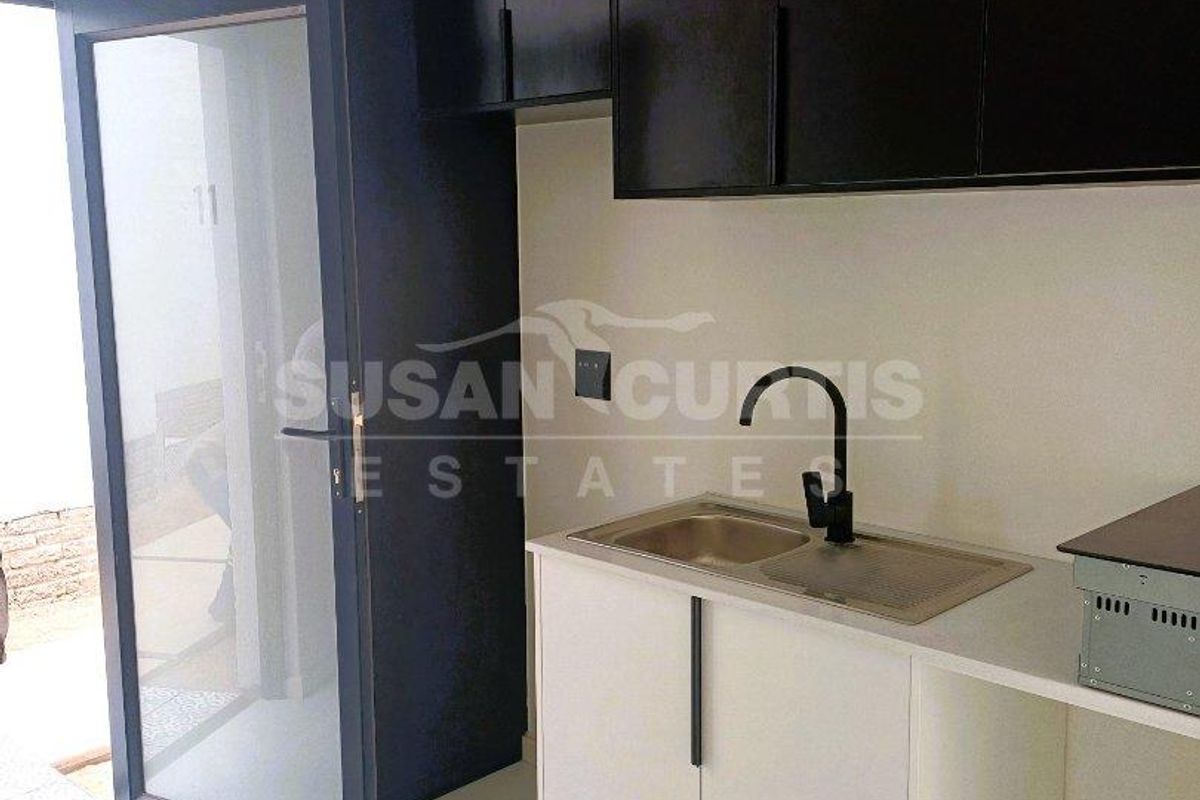 Compact kitchen area featuring modern dark upper cabinetry, white lower cabinets, a stainless steel sink with a black faucet, and direct outdoor access.