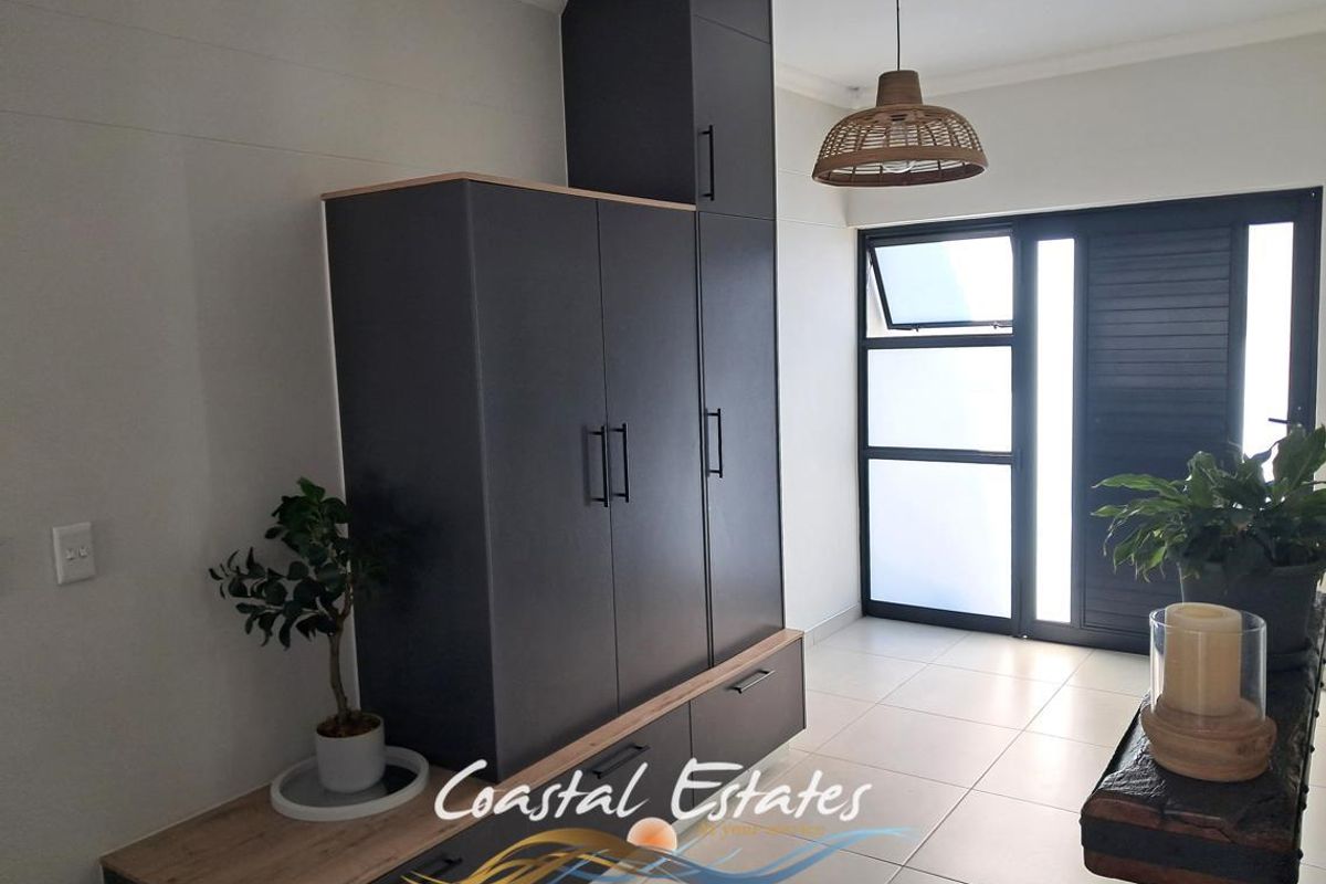 A modern living area featuring sleek dark built-in cabinetry, neutral tiled flooring, and a glass-paneled door providing natural light.