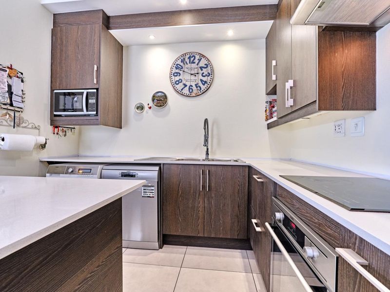 Modern kitchen featuring dark wood cabinetry, stone countertops, integrated appliances including an oven and cooktop, and tiled flooring.