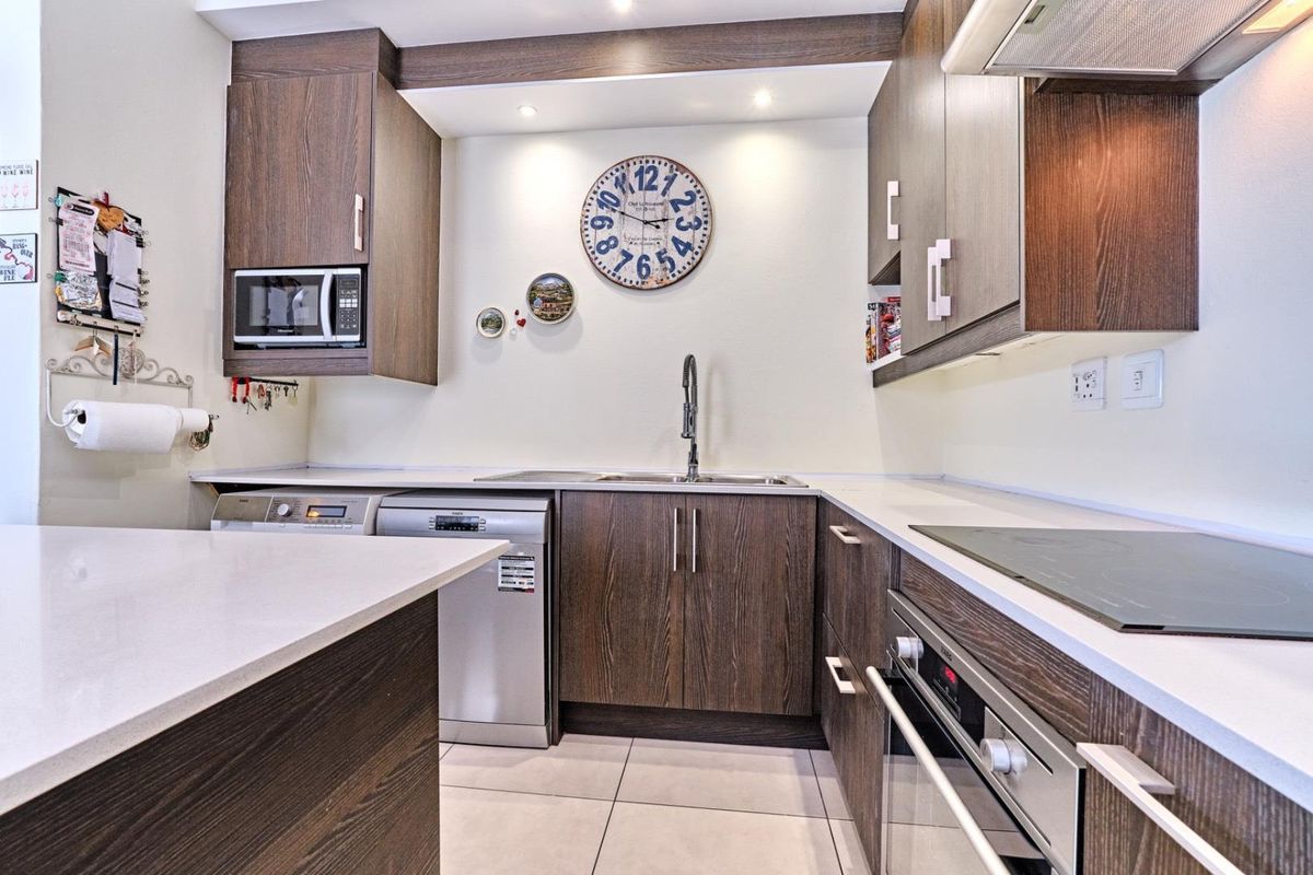 Modern kitchen featuring dark wood cabinetry, stone countertops, integrated appliances including an oven and cooktop, and tiled flooring.