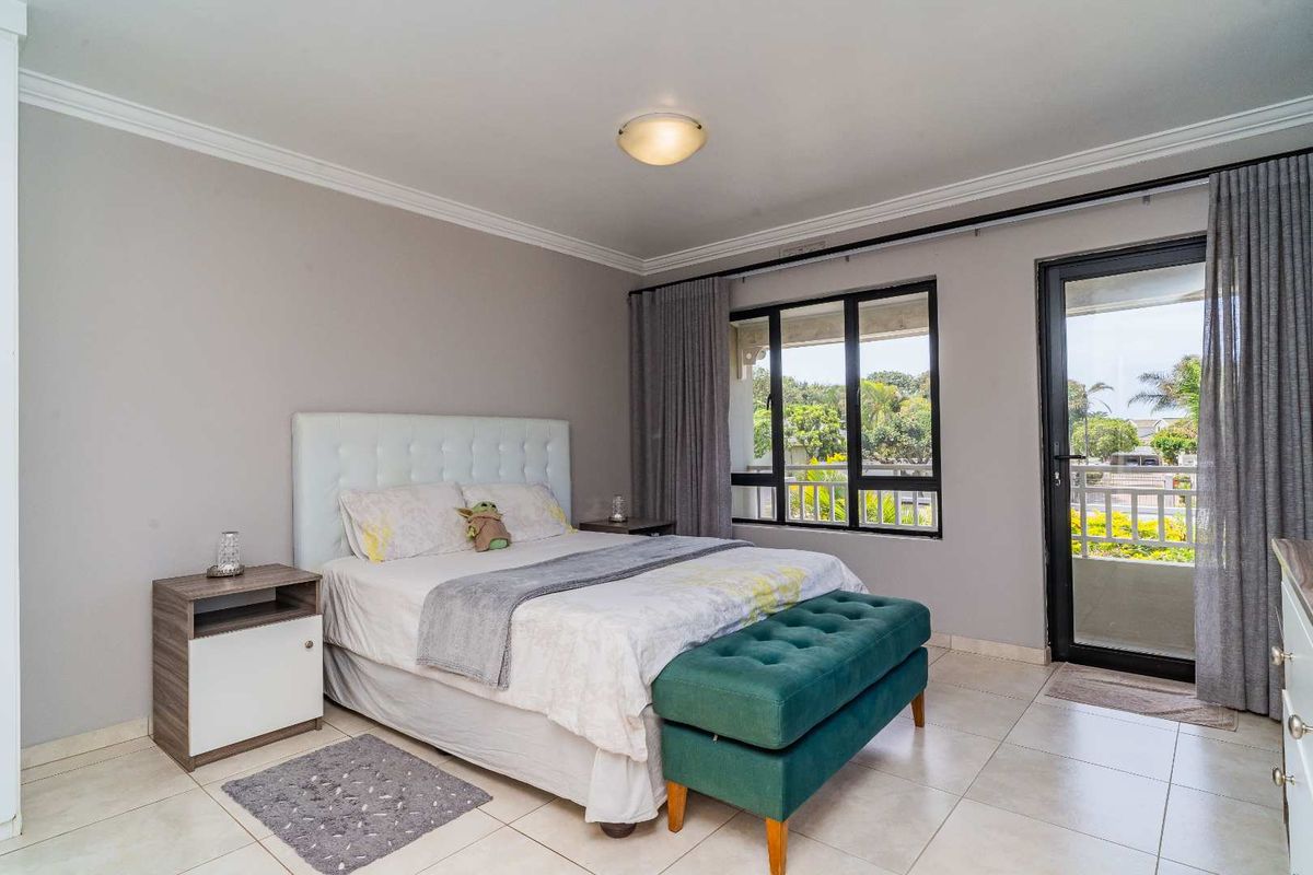 Spacious bedroom featuring tiled flooring, crown molding, and direct access to a private balcony through a glass door.