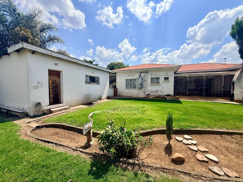 Rear view of the property featuring a spacious lawn, garden beds, and a detached outbuilding with a tiled roof.