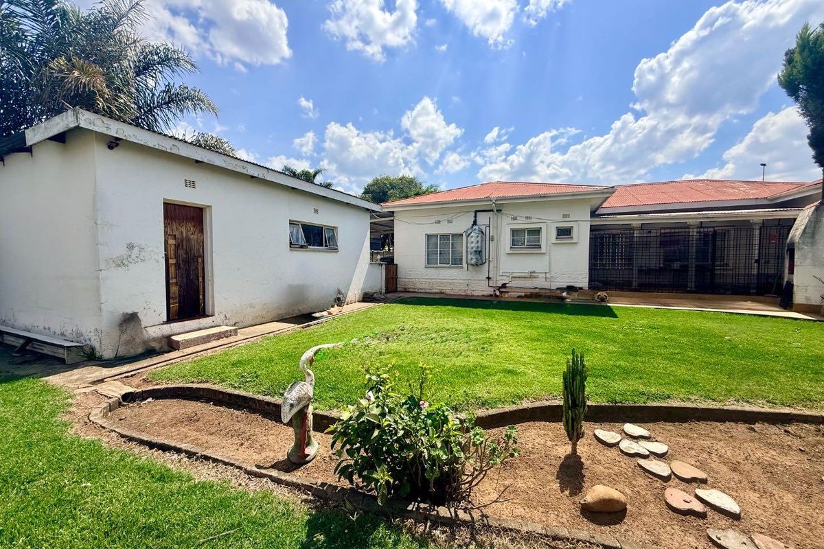 Rear view of the property featuring a spacious lawn, garden beds, and a detached outbuilding with a tiled roof.
