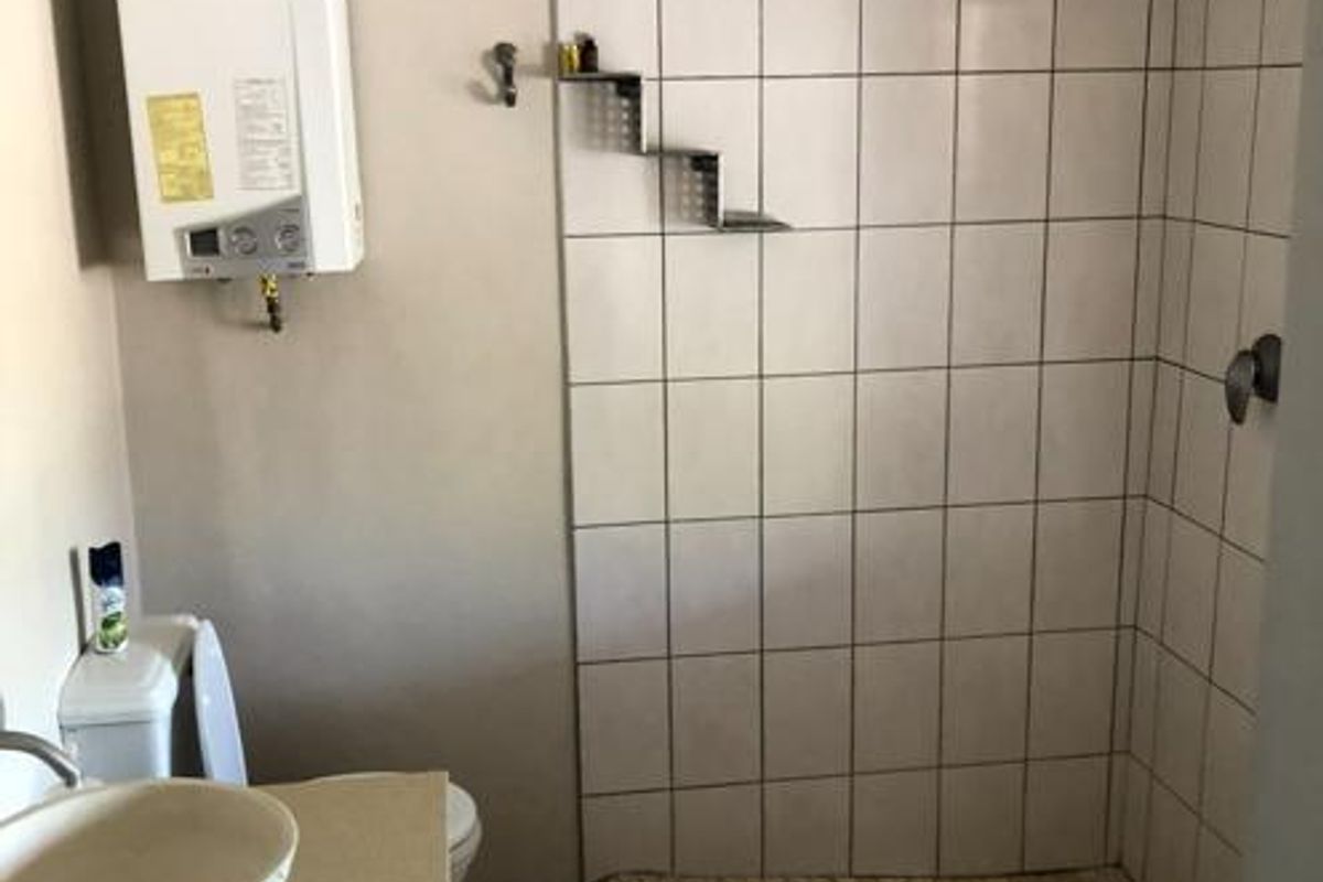 A functional bathroom featuring a vessel sink, toilet, and a tiled shower area with an exposed gas geyser unit.