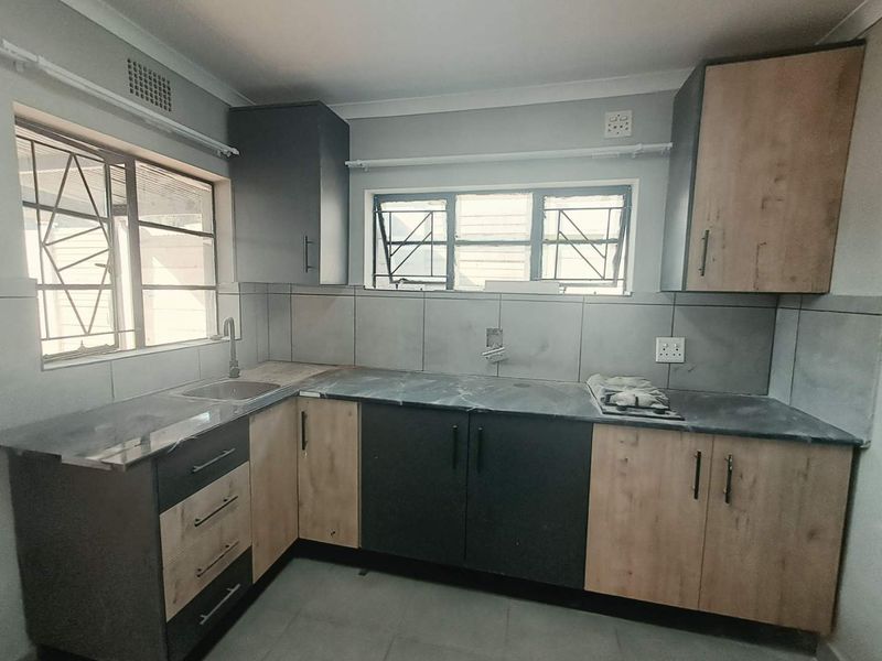 A functional kitchen featuring modern two-tone cabinetry, dark laminate countertops, a stainless steel sink, and a built-in hob with tiled splashbacks.