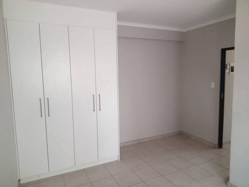 A clean, empty bedroom featuring neutral tiled flooring, white built-in cupboards, and a simple, modern interior finish.